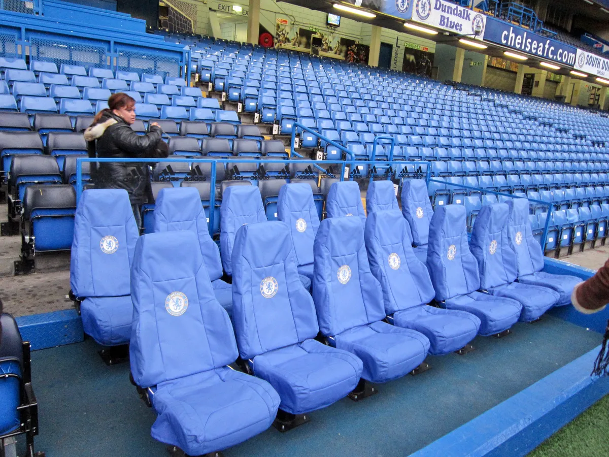 Padded blue dugout seats at pitchside on a Chelsea stadium tour at Stamford Bridge in London