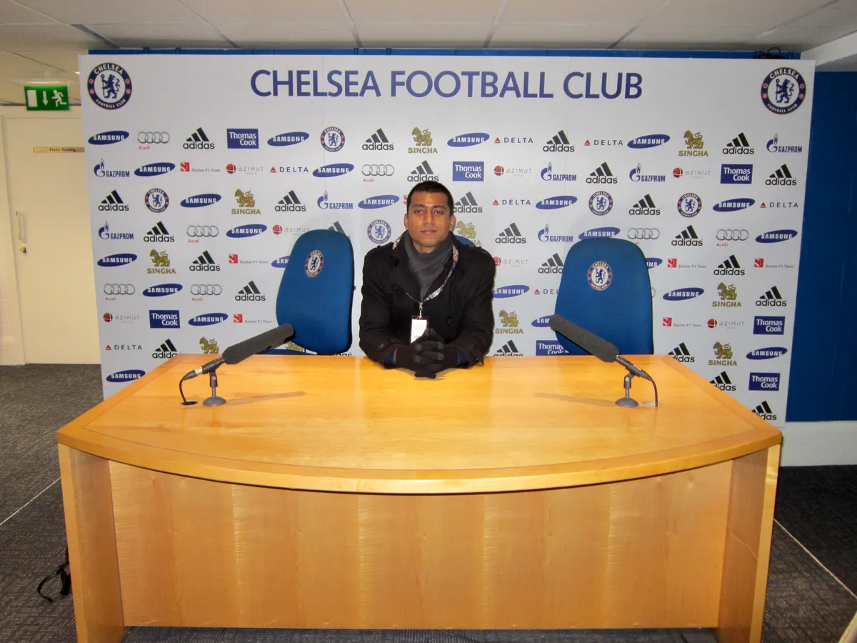 Visitor sitting behind the manager's desk in the press conference room on a Chelsea stadium tour